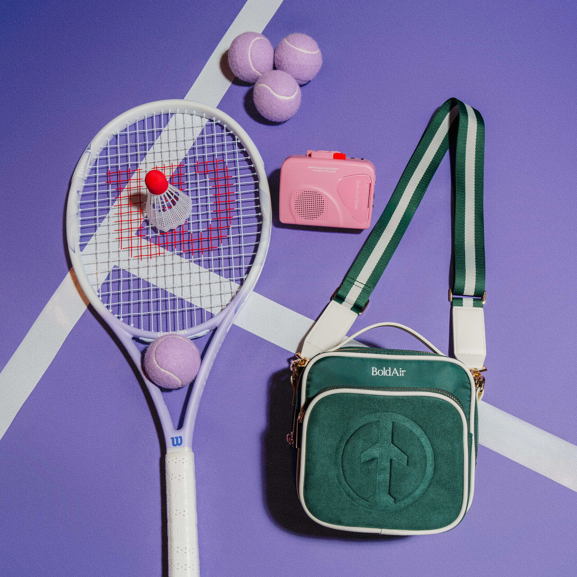 BoldAir Boarding Bag in green displayed with a tennis racket, tennis balls, and camera in a sporty lifestyle resort setting.