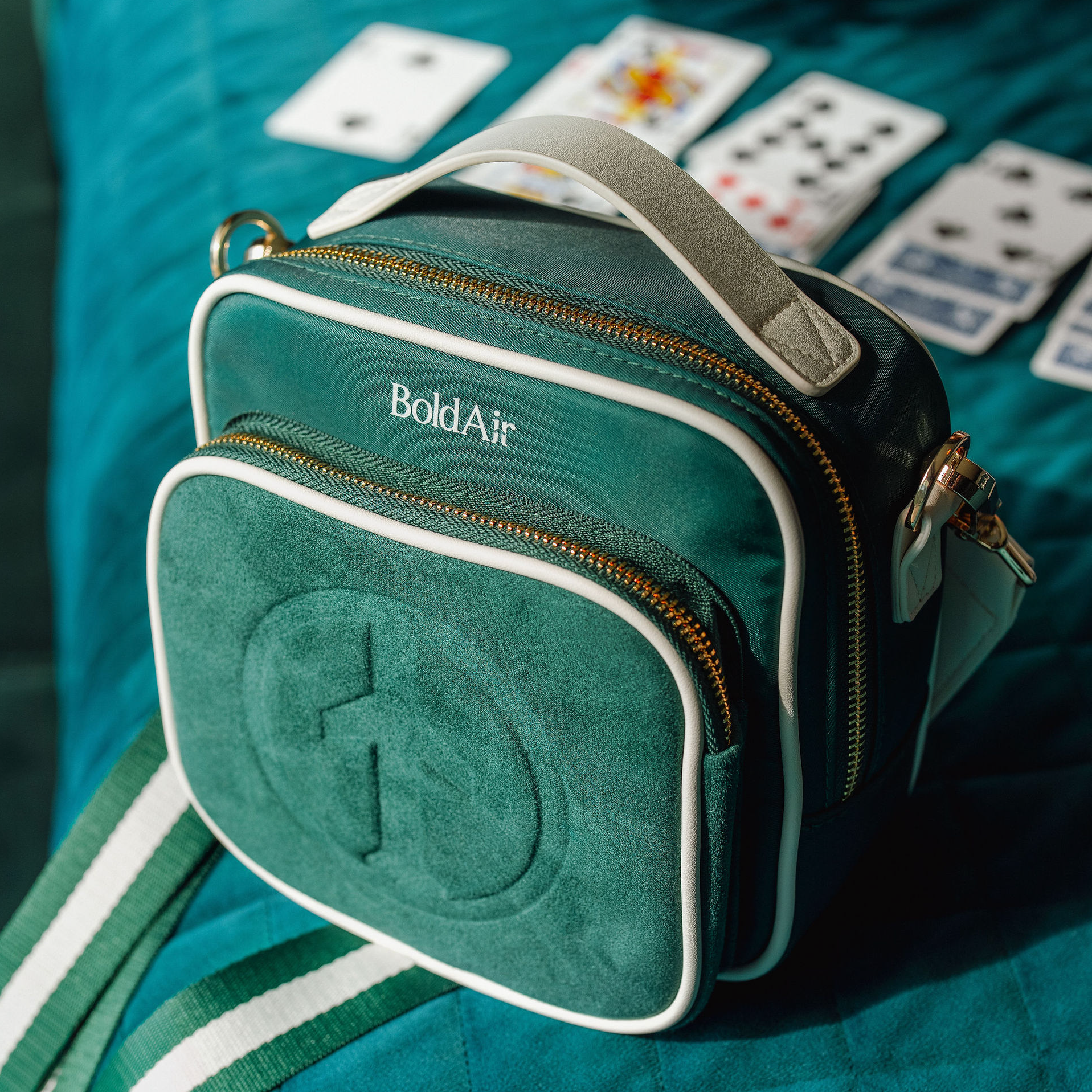 Green BoldAir Boarding Bag displayed on a hotel bed with playing cards, showcasing the crossbody travel bag in a hotel room setting.