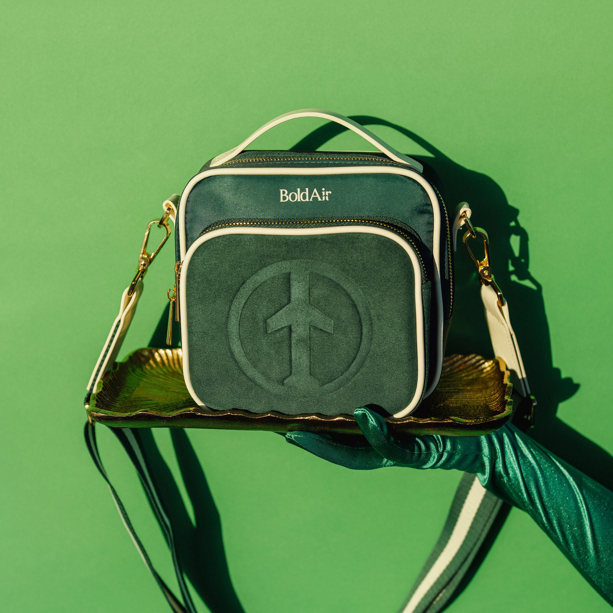 Green BoldAir Boarding Bag presented on a serving tray with a gloved hand, showcasing the crossbody travel bag in a luxury editorial setting.