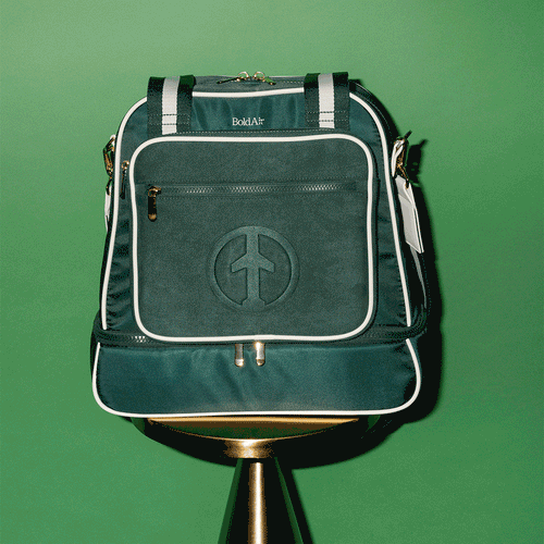 360 degree view of the green BoldAir Layover Bag with white piping, gold hardware, a dedicated shoe compartment, luggage sleeve, and adjustable shoulder strap.