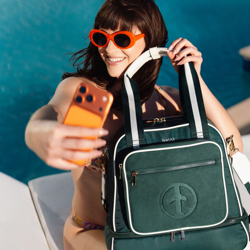 Woman taking a selfie by a resort pool with the green BoldAir Layover Bag, a women's overnight bag with white piping and gold hardware.