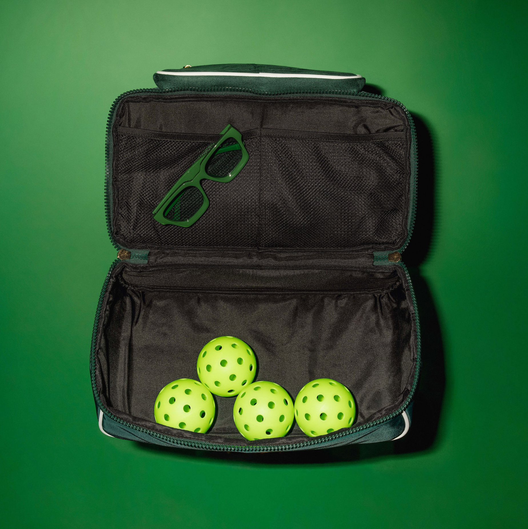Open shoe compartment of the green BoldAir Layover Bag filled with lime green pickleballs, showcasing the women's overnight bag in a sporty travel setting.